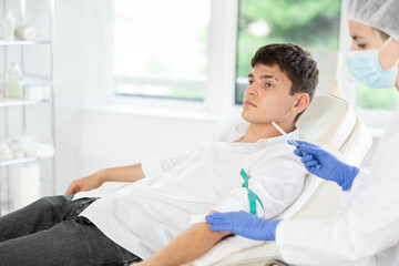 Young male patient having intravenously injection by nurse at treatment room of hospital
