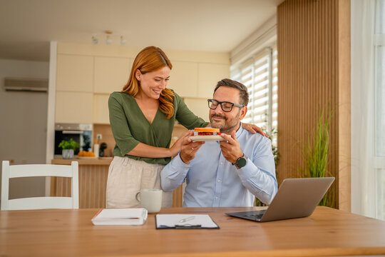 Woman bringing sandwich to man working from home - Powered by Adobe