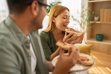 Happy couple enjoying pizza together at home, laughing