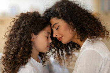 Side view of mother and daughter touching foreheads, moment of tenderness and caress. Family is love concept