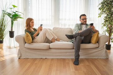 Couple ignoring each other focusing on smart phones on sofa