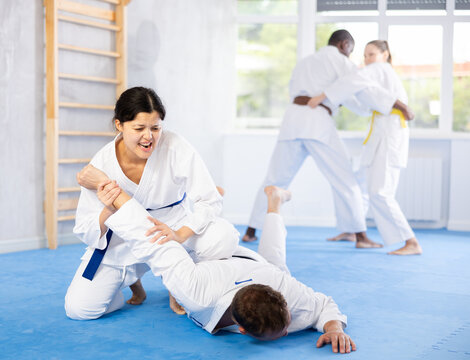 Adult man and young woman judokas practicing judo technique in group in gym