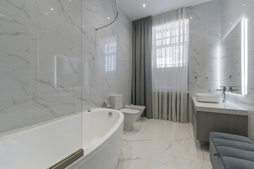 Stylish bathroom showcases sleek marble surfaces, a freestanding bathtub, and modern lighting. Natural light streams through a large window, enhancing the contemporary design.