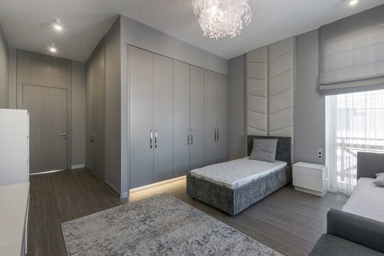 This modern bedroom showcases a minimalist design with gray furniture, ample storage, and a serene atmosphere. Natural light highlights the spacious layout, creating a calm retreat.