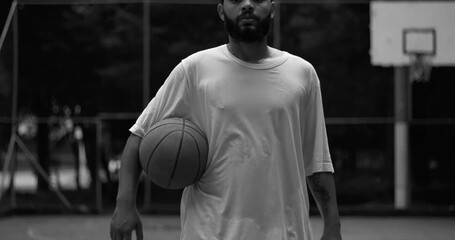 African American man on outdoor basketball court in black and white, holding ball under arm with confident posture, representing strength, focus, and calm determination