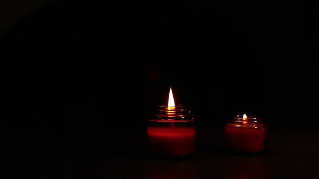 Two decor mood design burning aroma candles in elegant brown glass on dark black background in holiday Christmas night. Aromatic decoration lighting objects in the room on the table