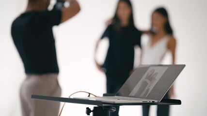 Photographer taking pictures of models in photo studio with laptop