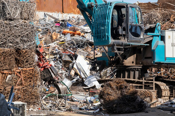 Excavator loading scrap metal onto truck in junkyard. Industrial excavator working at metal recycling yard. Excavator handling metal waste at recycling facility.