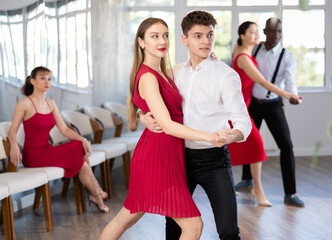 Fototapeta premium Smiling couple enthusiastically dancing social latin cha-cha-cha dance in modern dance salon