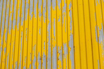 Weathered industrial wall with faded ytellow paint. Aged yellow painted wall texture. Peeling yellow paint on metal wall.