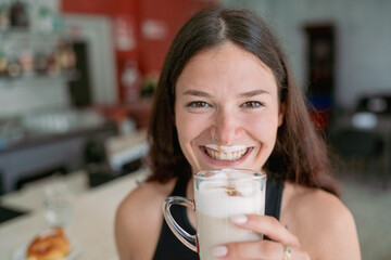 Joyful Young Woman Enthusiastically Enjoys a Refreshing Latte Macchiato While Holding the Glass...