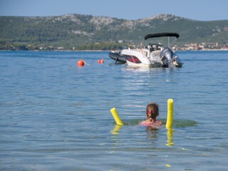 Naklejka premium little girl swims using foam noodle in seawater on a beach in Croatia