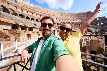 Smiling mixed race couple taking a selfie with colosseum in background during their roman vacation,...