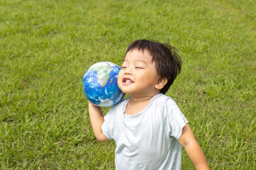 地球儀を持って草原で立っている男の子（2歳、日本人、笑顔）