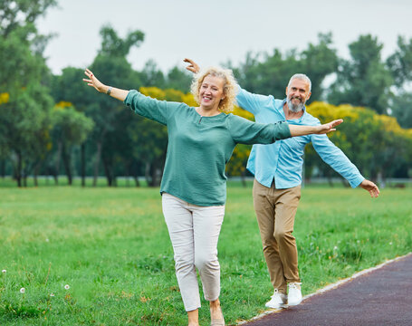 Happy active mid aged adult couple having fun walking and balancing and bonding in park or nature outdoors, healhty active mature people exercise concept