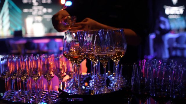 The waiter pours white wine into the glass. Sommelier waiter pouring white wine into glasses at indoor party. A waiter pours white wine into glasses in a restaurant. - Powered by Adobe