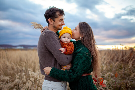 Young family couple holding baby girl walking on fall meadow. Stylish mom, dad and daughter wearing warm fall clothes.