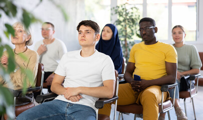 Focused young guy participating study session, sitting in auditorium with group of women and men on...