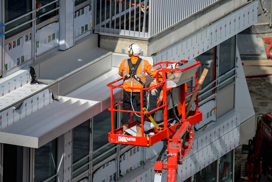 Des ouvriers du b&acirc;timent sur une nacelle installant des mat&eacute;riaux sur l'ext&eacute;rieur d'un immeuble