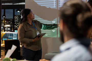 Multiethnic business consultants review feedback and targets to work on future project, developing a plan and strategy during night time meeting. Company associates in dark office.