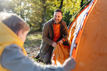 Dad proudly watching boy help with assembling tent
