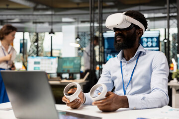 African American executive wears VR headset and holds controllers during interactive meeting on business analytics. Black man financial planning using virtual technology in modern office.
