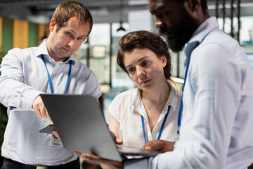 Fototapeta premium Diverse employees in modern office, drafting reports and collaborating on strategic planning. Multiethnic professionals reviewing data on laptop to support business progress and innovation.