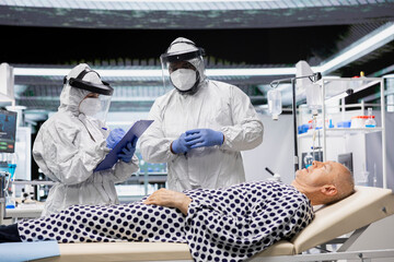 Scientific research team in quarantine examines old man under biohazard conditions, recording treatment outcomes and immune response to support innovation and science in epidemic prevention.