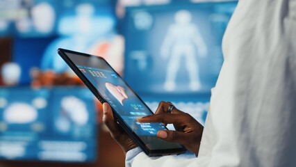 Close up of researcher analyzing human anatomy using tablet app in front of digital health dashboards backdrop. Scientist zooming on touchscreen device display keyboard, analyzing medical scans