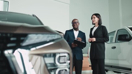 African American man in a suit discussing car features with a woman in a stylish outfit at a modern dealership, showcasing the car buying experience and customer service