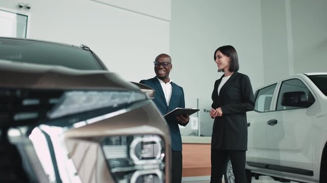 A female buyer and male salesperson discuss vehicle specifications in a dealership showroom, demonstrating customer interaction and the buying experience in the modern automotive environment.