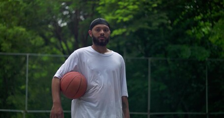 African American man posing with basketball on outdoor court, composed and confident stance reflecting focus, preparation, and passion for the game