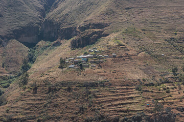 Obraz premium A small, remote village nestled on a steep, arid mountainside in the Andes of Peru. Agricultural terraces are visible on the slopes, showing traditional rural life in South America.