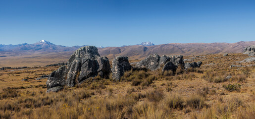 Striking view of the Hatun Machay stone forest in Ancash, Peru. Massive, eroded rock formations stand in a high-altitude Andean landscape, with the snow-capped Cordillera Blanca in the distance.