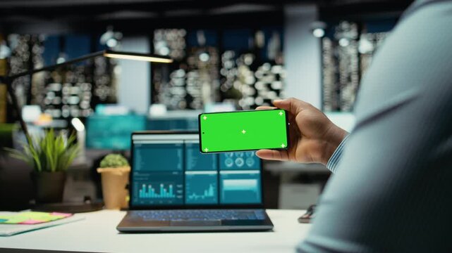 African american man working with green screen on mobile phone in modern space, checking online insights in strategy room. Male general manager handling business administration. Camera A.