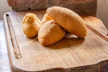 Four pieces of rustic bread with golden crust on wooden cutting board, featuring round and oval shapes in cozy homemade baking scene with textured background.