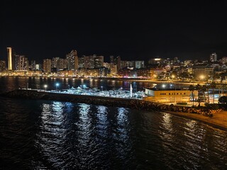 Obraz premium bright promenade with water reflections, city skyline illuminated by glittering lights by water