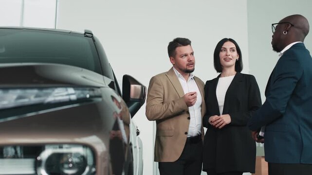 Happy couple discussing car purchase with dealership representative, showcasing modern vehicle features and professional atmosphere in a bright showroom with copy space - Powered by Adobe