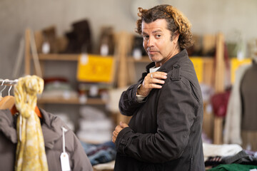Man stands in the interior of a store and tries on a black windbreaker. Buying outerwear for a cold autumn