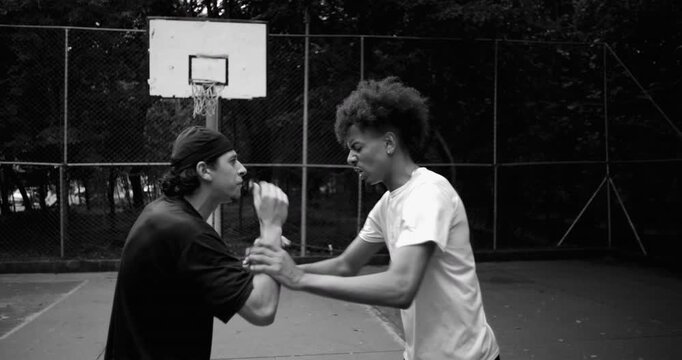 Hispanic and African descent men arguing on outdoor basketball court, escalating tension as emotions rise, aggressive gestures and shoving intensify
