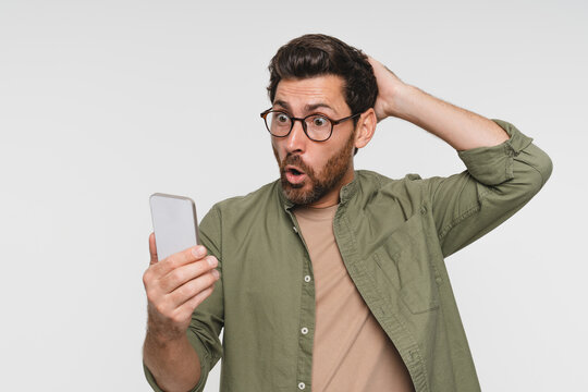 Head shot portrait shocked man looks at screen open mouth make big eyes holds phone astonished by received sms feels stunned surprised amazed pose studio white wall, unbelievable news concept