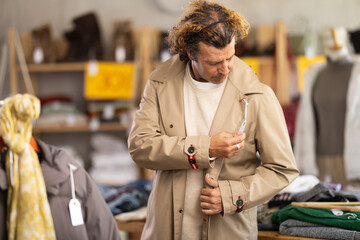 Adult man tries on a beige coat trench coat in a clothing store, he looks at the quality of the material and his size. Buying and trying on outerwear in the showroom