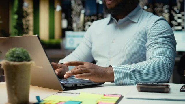 Close up of black worker proofreading and fact checking financial data, reviewing archived files after hours in strategy room. Evaluating reports, researching and organizing agenda. Camera A.
