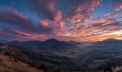 Vibrant sunset paints the sky over majestic mountain range and valley.