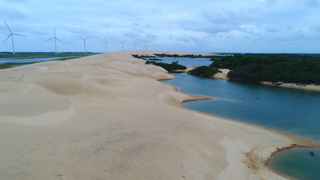 Imagem a&eacute;rea de drone dos Pequenos Len&ccedil;&oacute;is Maranhenses em Paulino Neves, Maranh&atilde;o, com dunas de areia branca, lagoas azuis e parque e&oacute;lico ao fundo