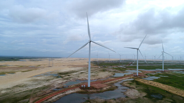 Vista a&eacute;rea dos Pequenos Len&ccedil;&oacute;is Maranhenses em Paulino Neves, Maranh&atilde;o, com dunas, lagoas e torres e&oacute;licas sob c&eacute;u azul ensolarado, capturada por drone