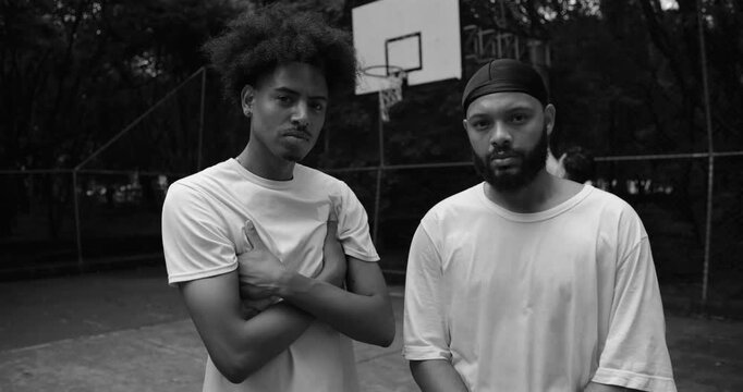 Two African American men standing side by side with arms crossed on outdoor basketball court, confident serious expression, unity and strength after heated game