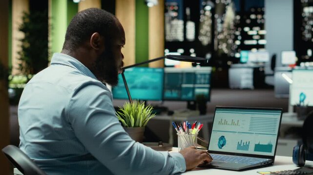 Black business consultant working late at night on proofreading documents, writing reports on laptop. Creating a summary and designing strategy to align with company objectives. Camera B.