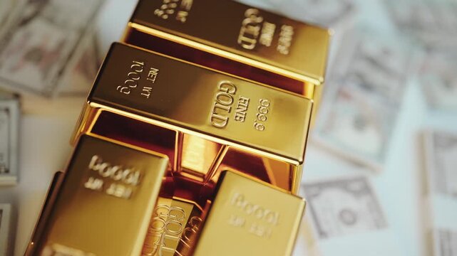 Stacks of pure gold ingots laying on a background of american dollar banknotes, representing a concept of wealth, investment security, financial success, and precious metal trading