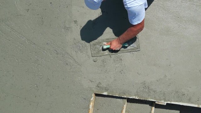 Construction worker are using finishing trowels on freshly poured concrete to create a smooth, level surface at a building site. View from above shows worker leveling the surface of the stairs